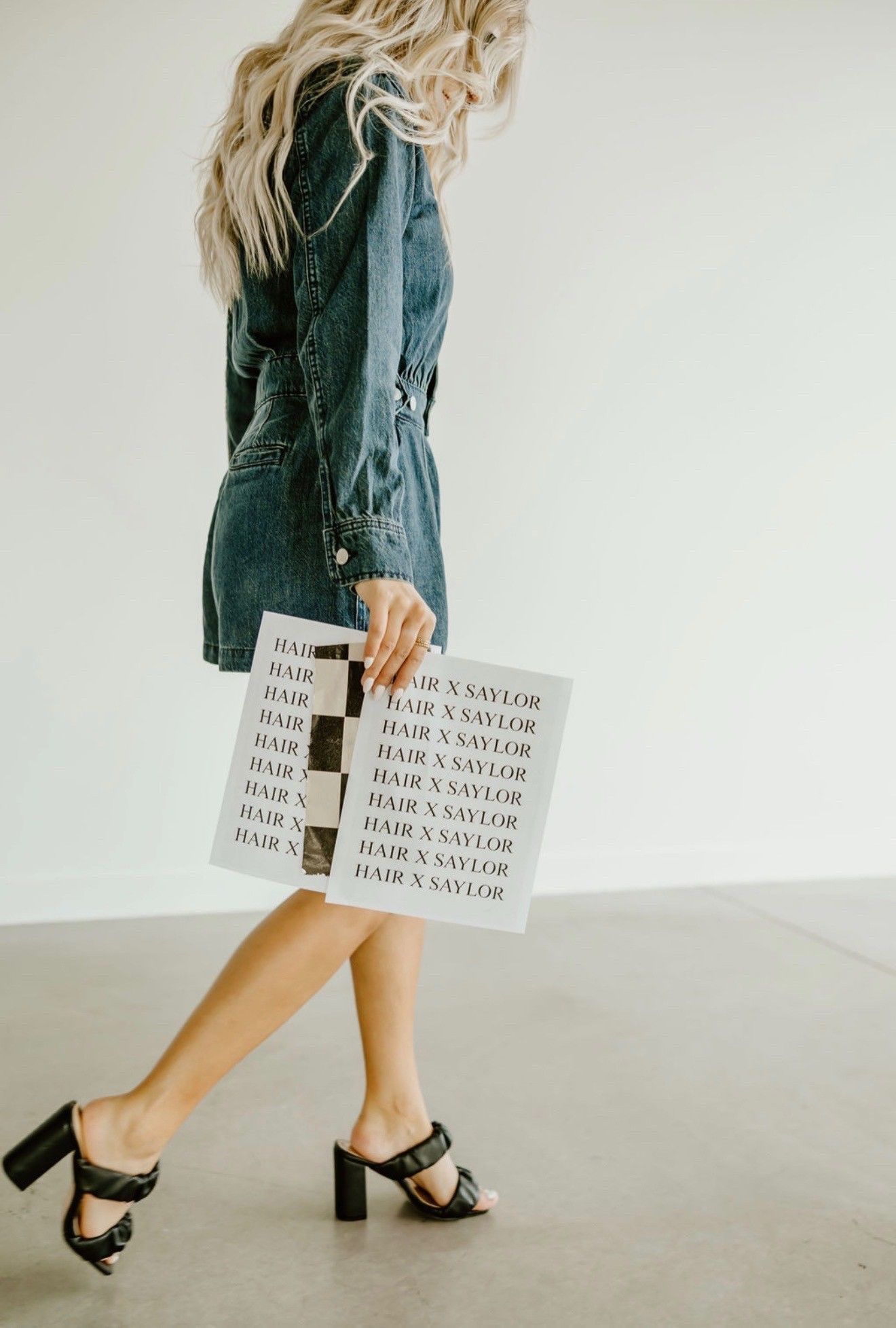 Woman in a dark green dress walking in black heels, carrying a white tote bag with text.