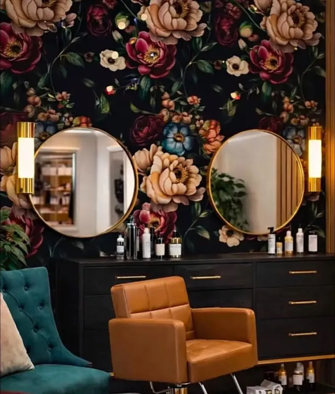 Elegant salon interior with floral wallpaper, round mirrors, warm wall lights, and teal and tan chairs.