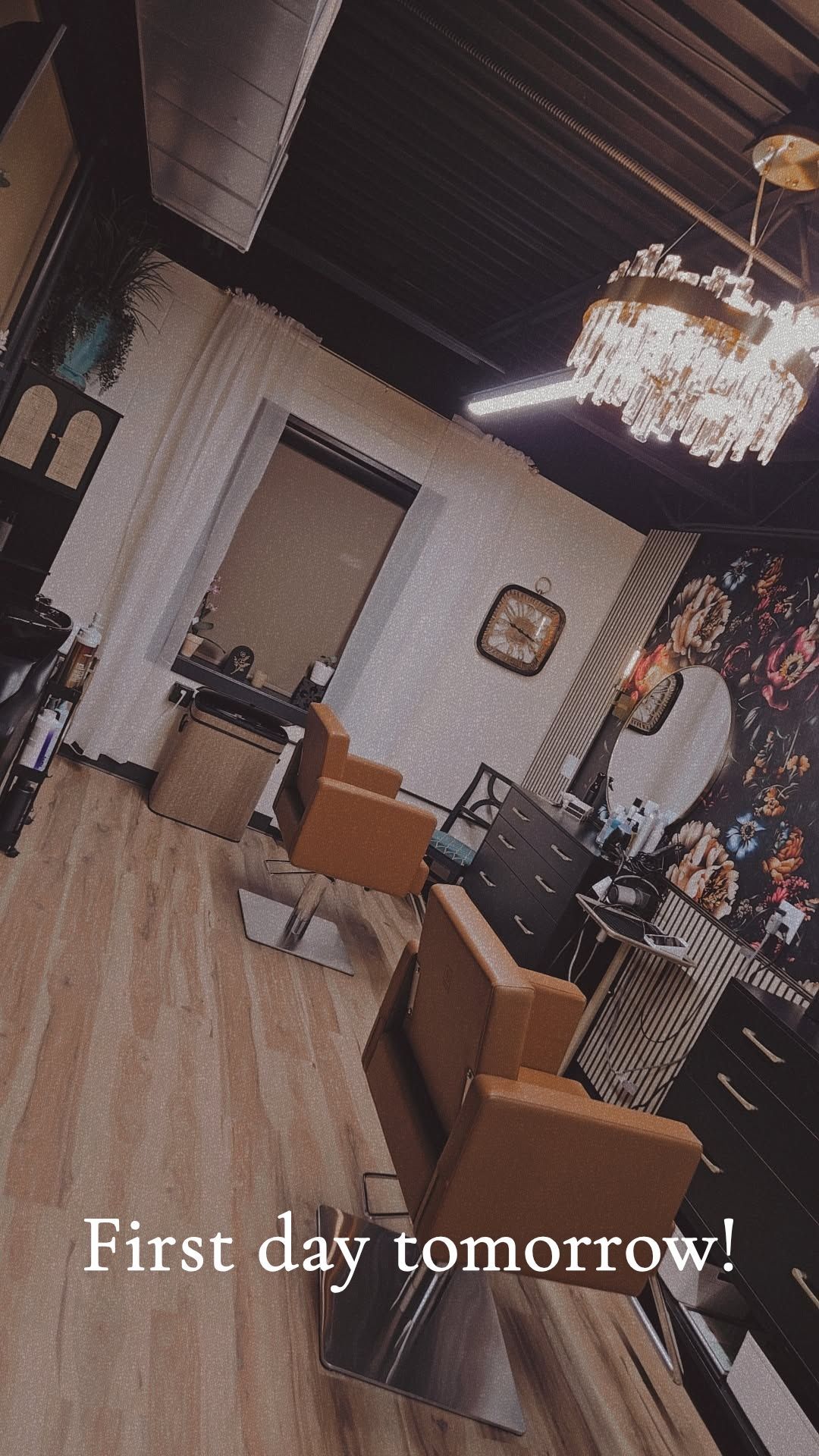 Elegant salon interior with chandelier, wood floors, mirror, styling chair, and caption “First day tomorrow!”