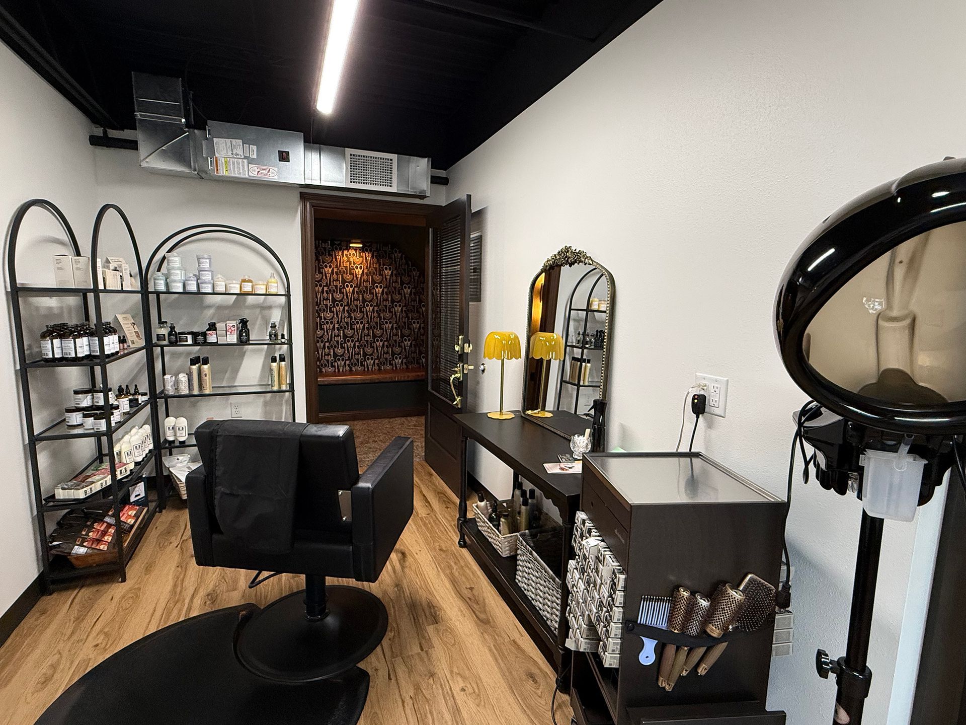 Modern salon interior with styling chair, mirrors, black shelving, and hair-washing station