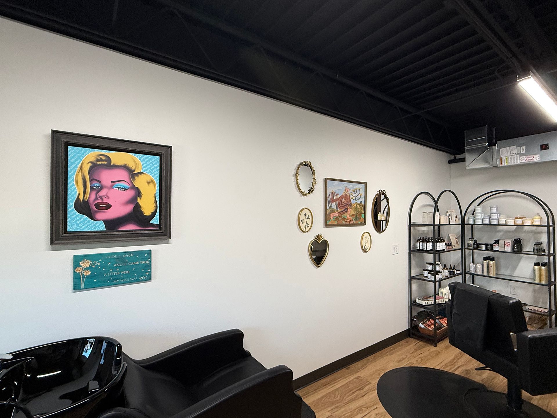 Modern salon interior with art on white walls, black chairs, shelves, and a wood floor