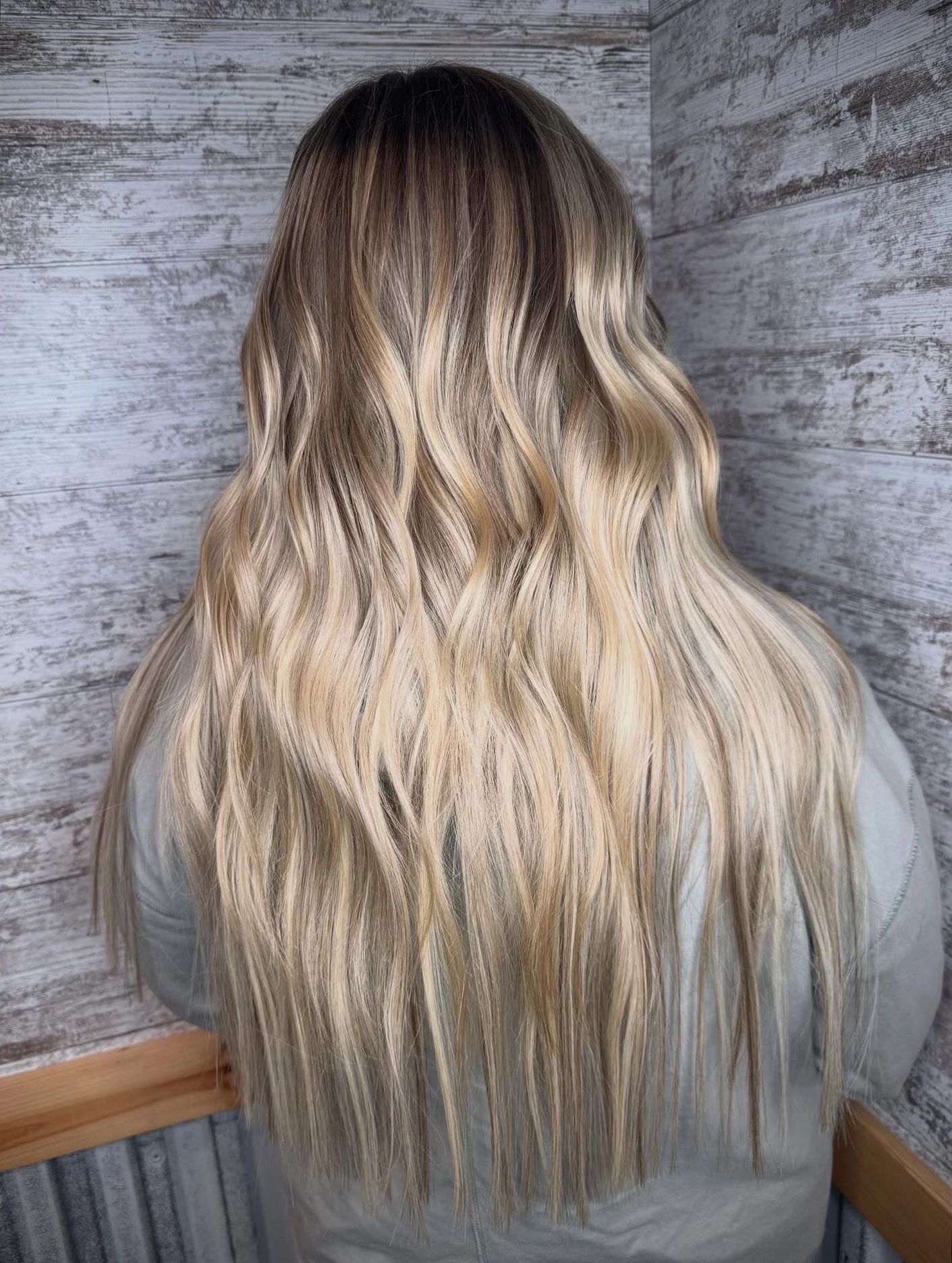 Long wavy blonde ombré hair shown from the back against a textured gray wall