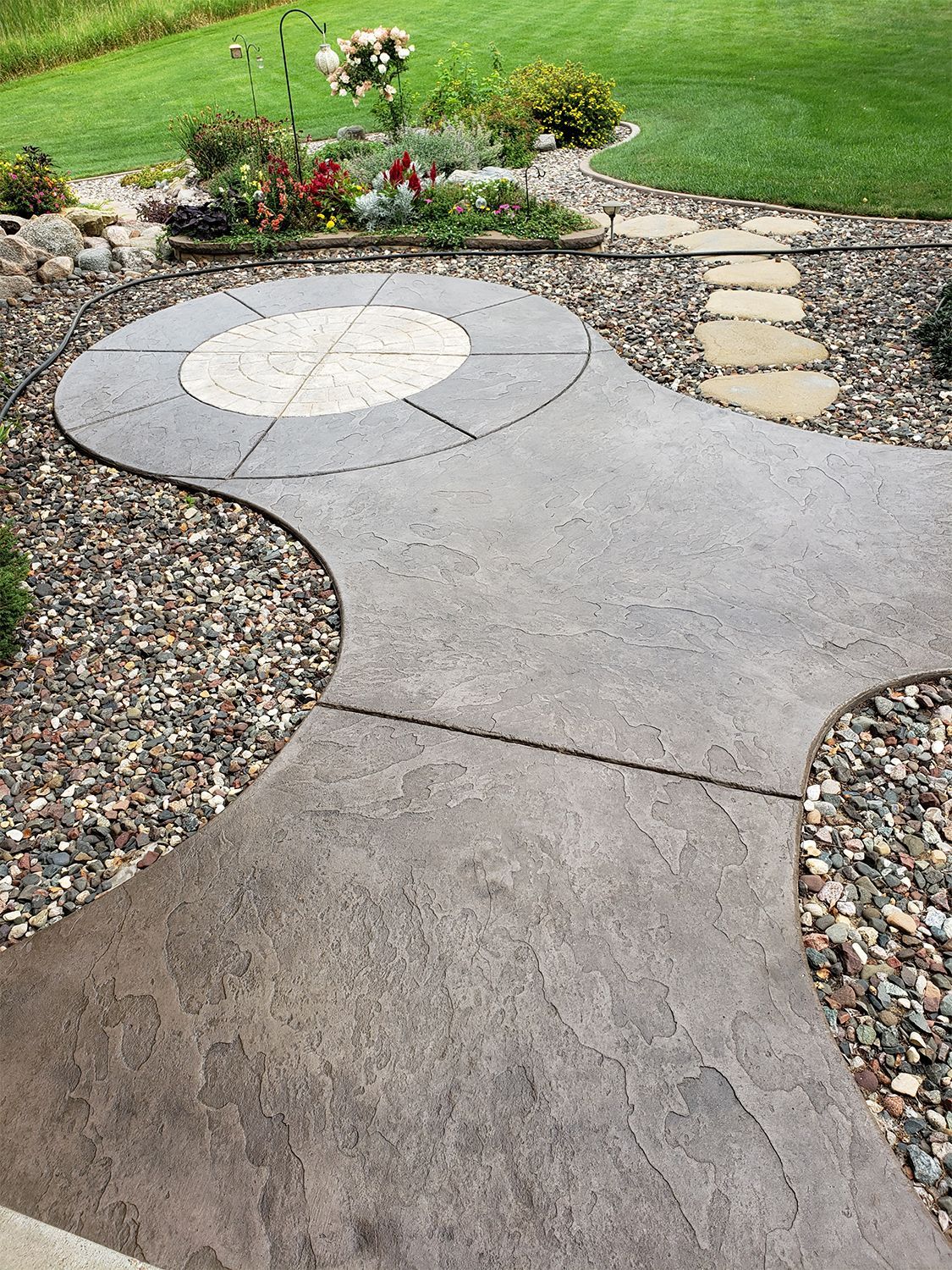 A concrete walkway surrounded by rocks and flowers in a backyard.