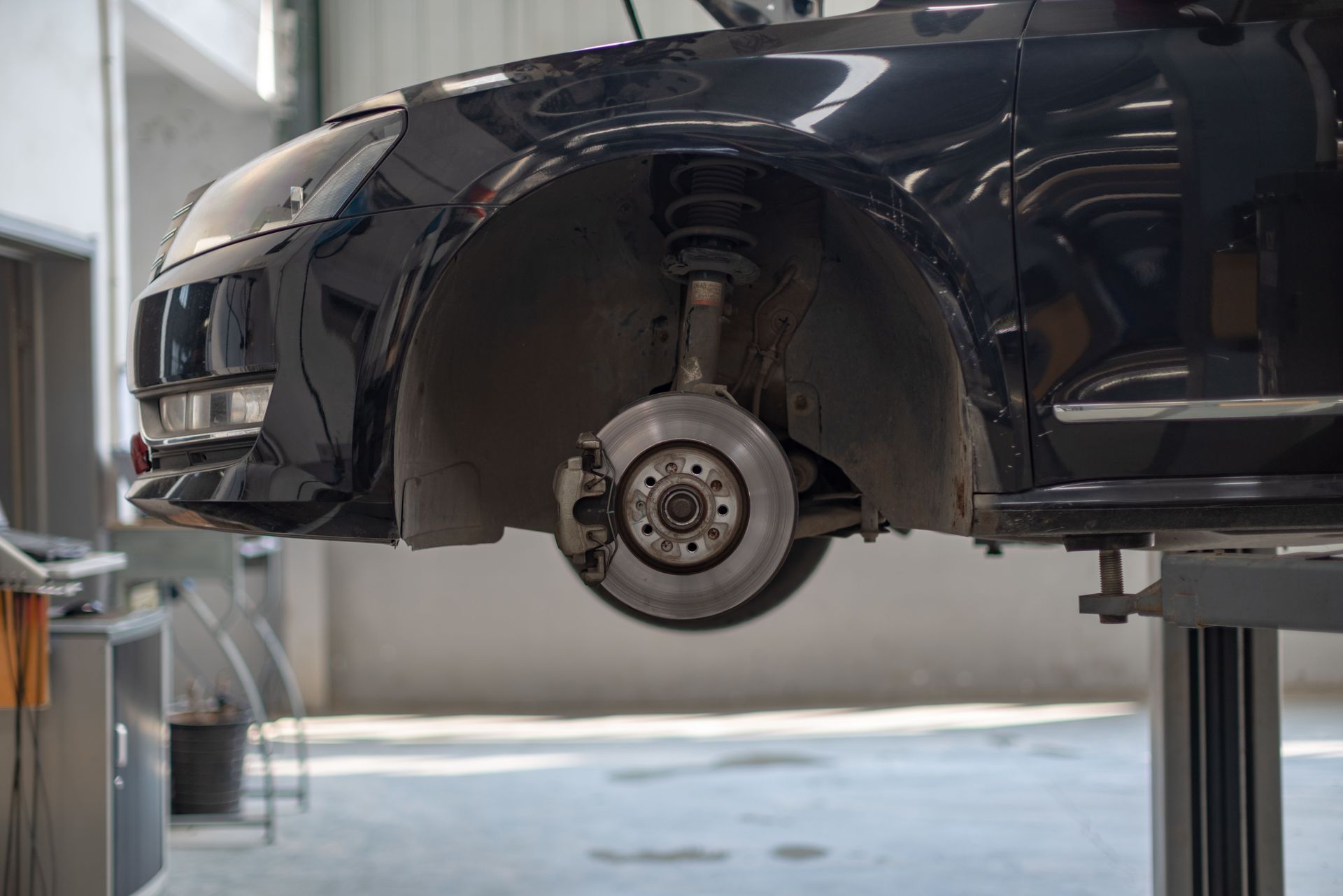 Black car lifted on a shop hoist, showing the exposed front wheel hub and brake assembly.