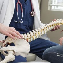 A doctor with a stethoscope around his neck is holding a model of the spine