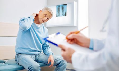 A man is sitting on a bench talking to a doctor who is holding a clipboard.