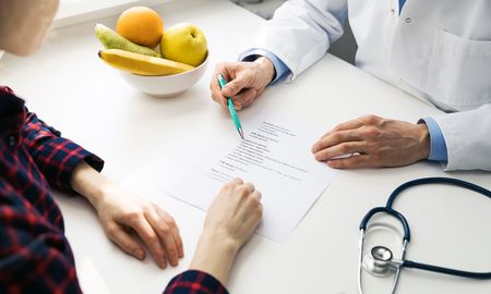 A doctor is talking to a patient who is sitting at a table with a bowl of fruit.