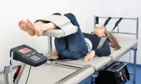 A woman is laying on a bed with her legs up and a machine on her feet.