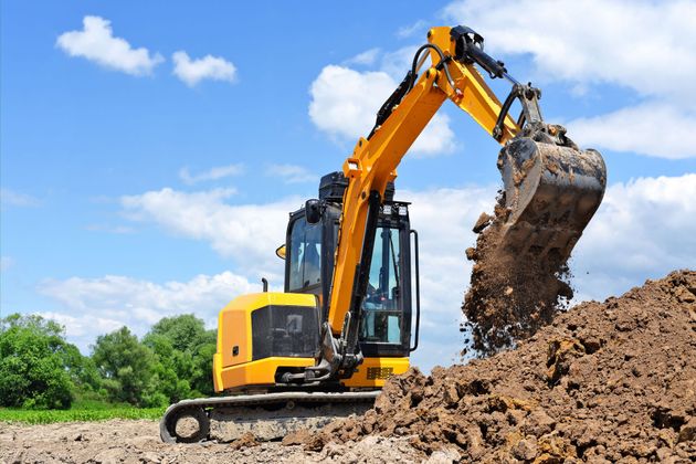 Yellow excavator digging dirt at a construction site under a blue sky.