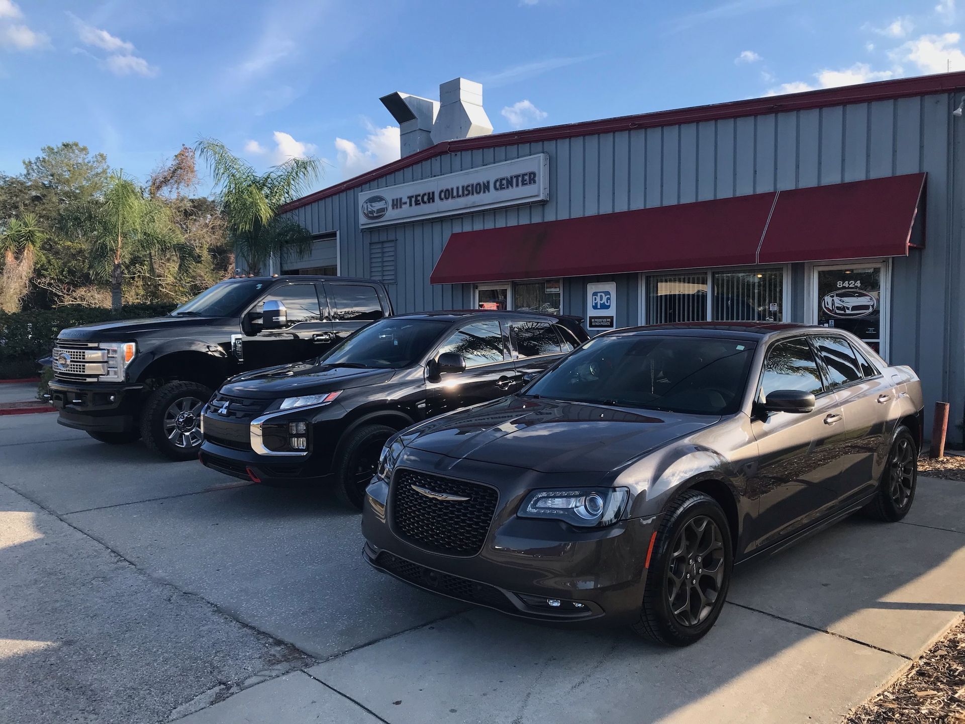 Three cars parked in front of a business. The building is gray with a red awning and sign above the door.
