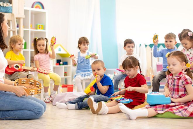 Children in a classroom, playing musical instruments with a teacher.