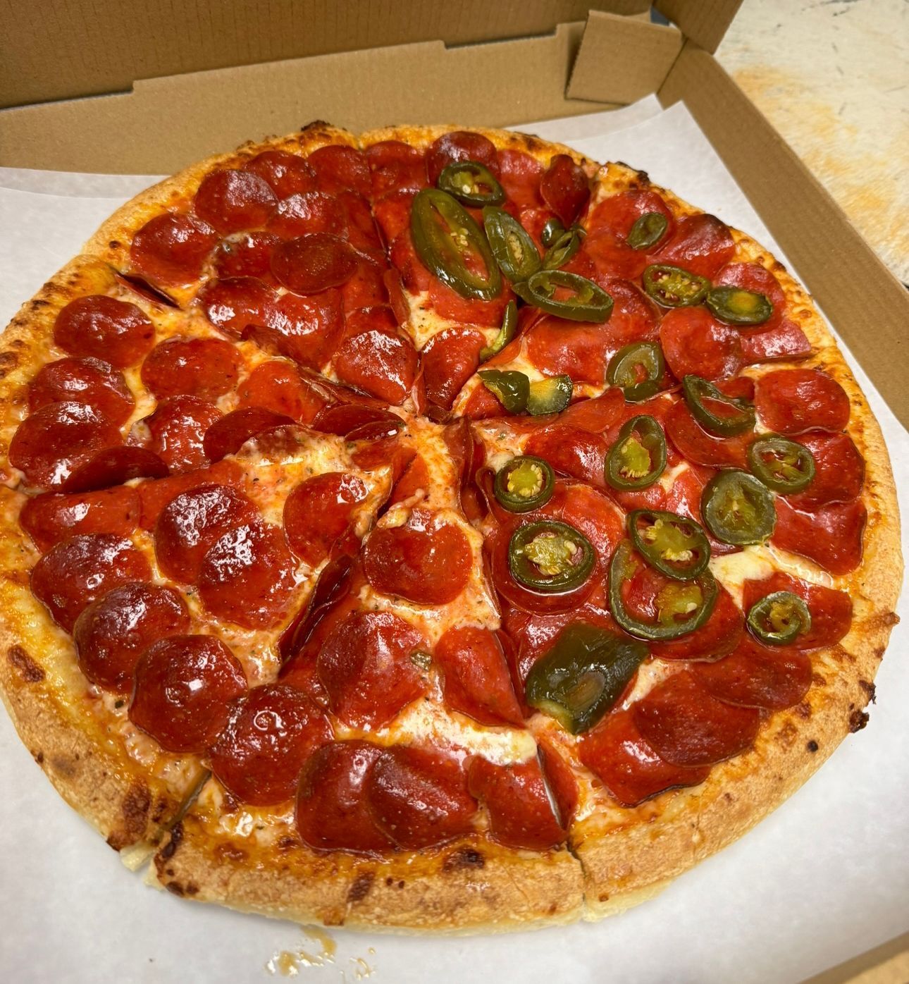 A pepperoni pizza with jalapenos is in a cardboard box