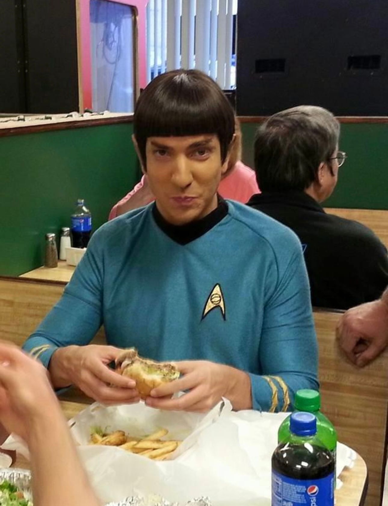 A man in a star trek uniform is eating a hamburger