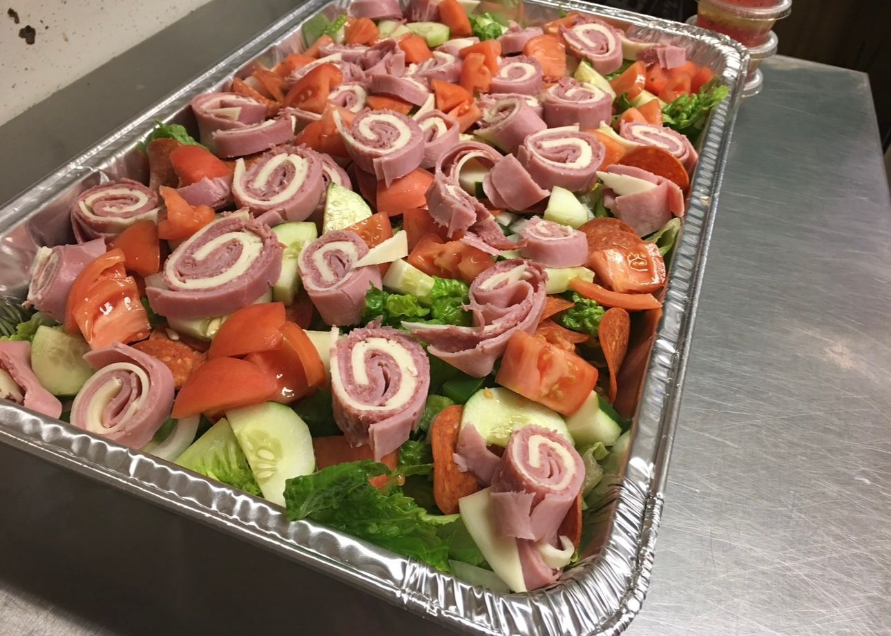 A tray of food with tomatoes , cucumbers , and ham on a table.