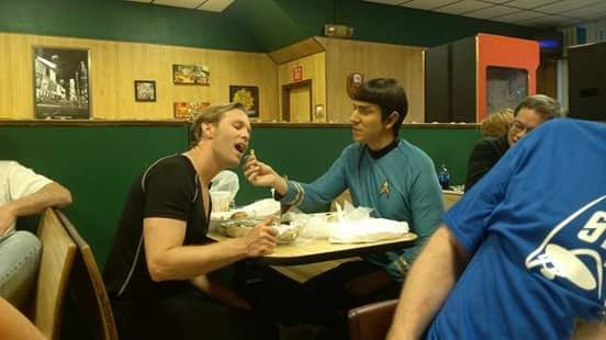Two men are sitting at a table in a restaurant eating food