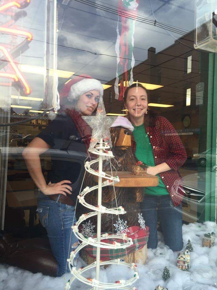 Two women are standing in front of a christmas tree in a store window.