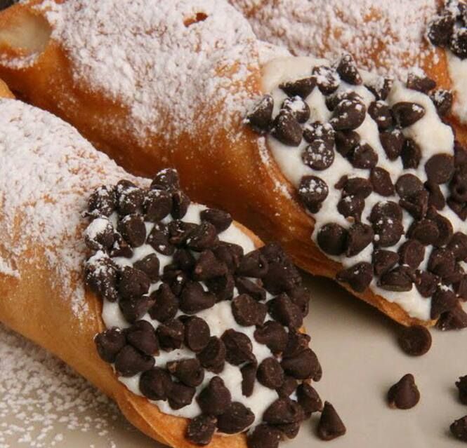 A close up of a cannoli with chocolate chips and powdered sugar