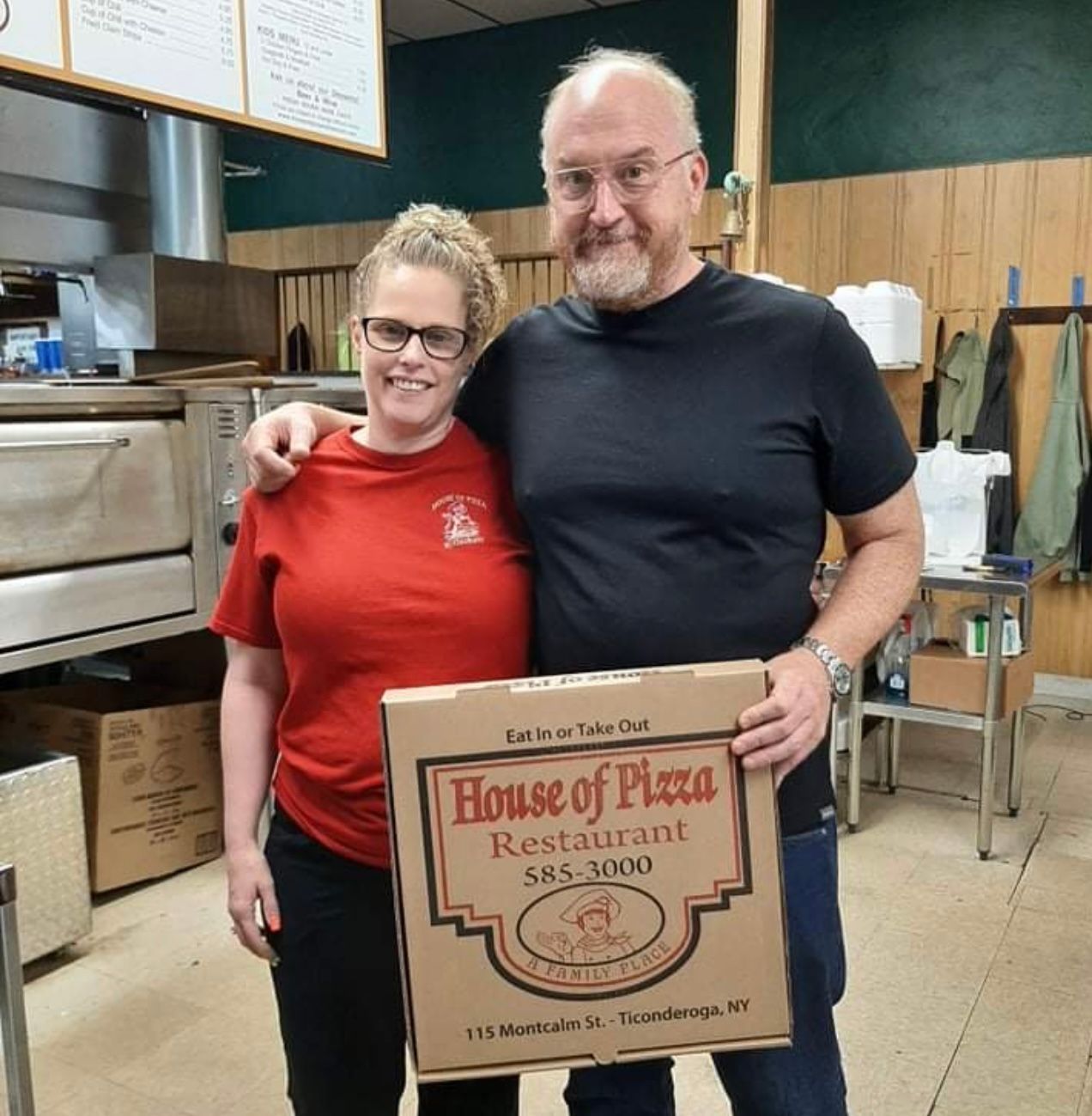 A man and a woman are posing for a picture with a box that says house of pizza restaurant