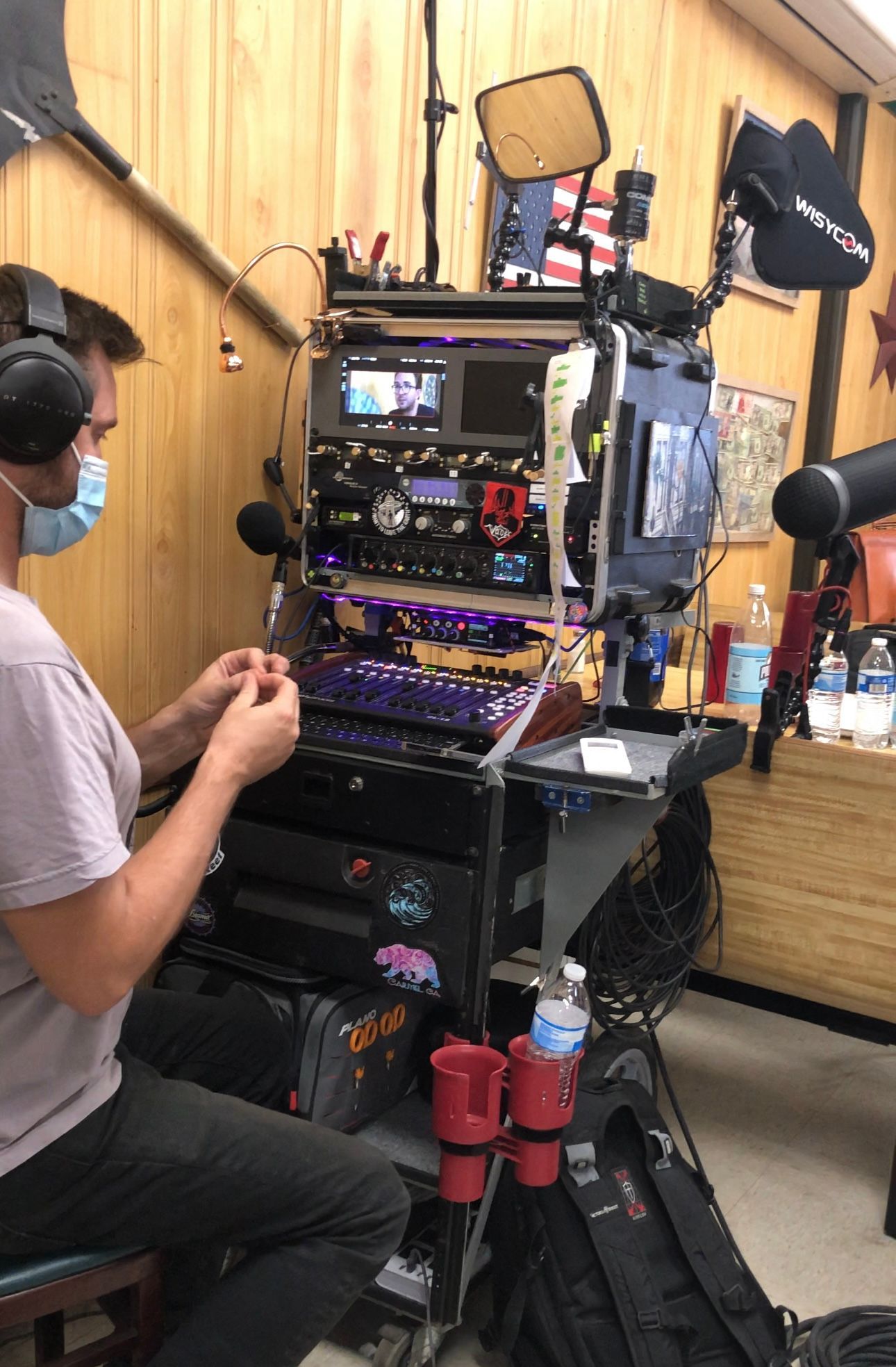 A man wearing a mask is sitting in front of a microphone in a room.