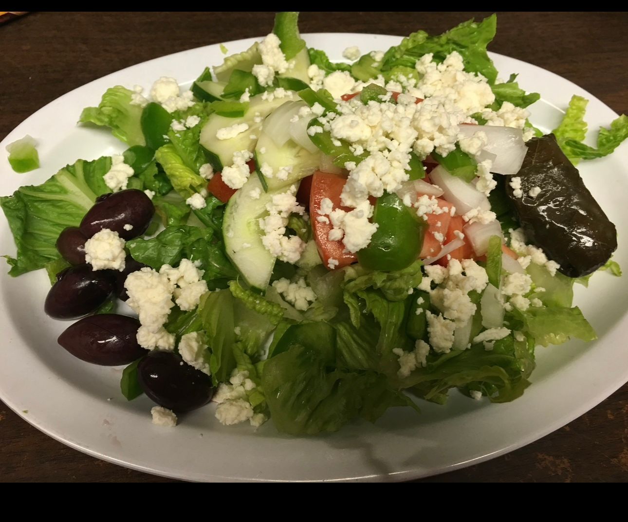 A white plate topped with a salad and olives