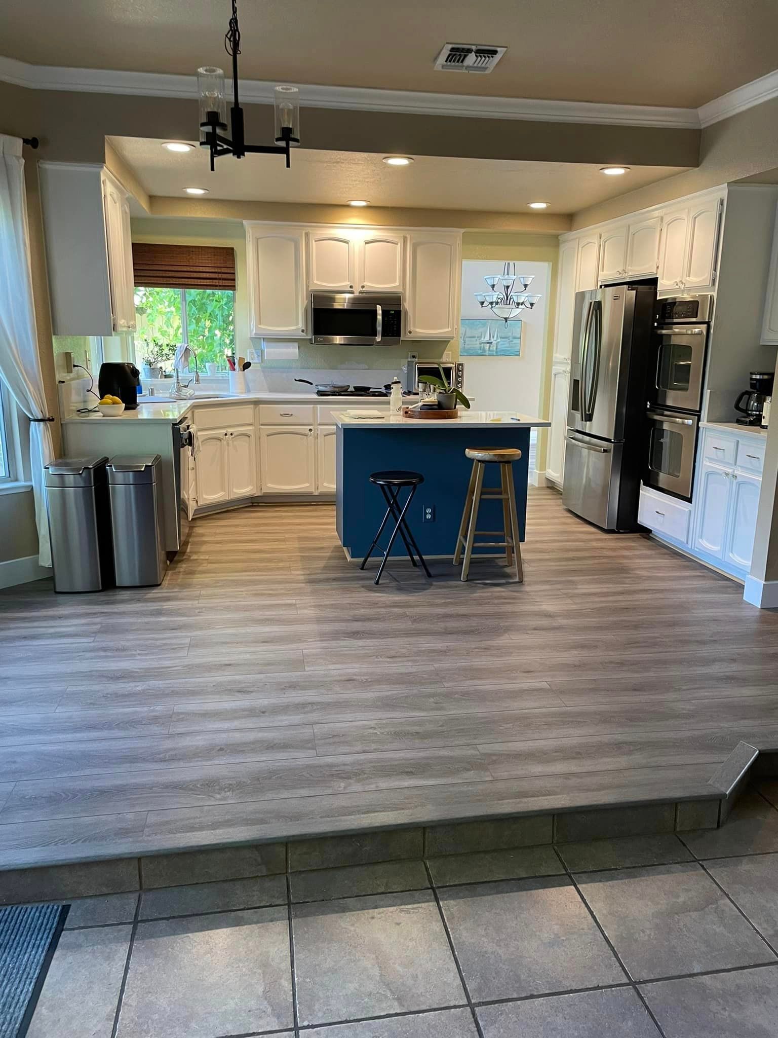 A kitchen with white cabinets , stainless steel appliances , and a blue island.