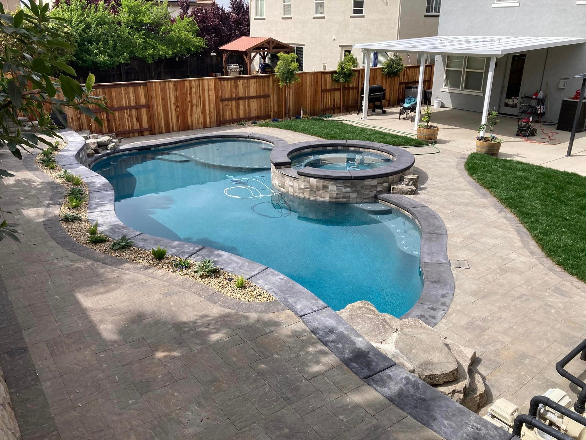 A large swimming pool with a hot tub in the backyard of a house.