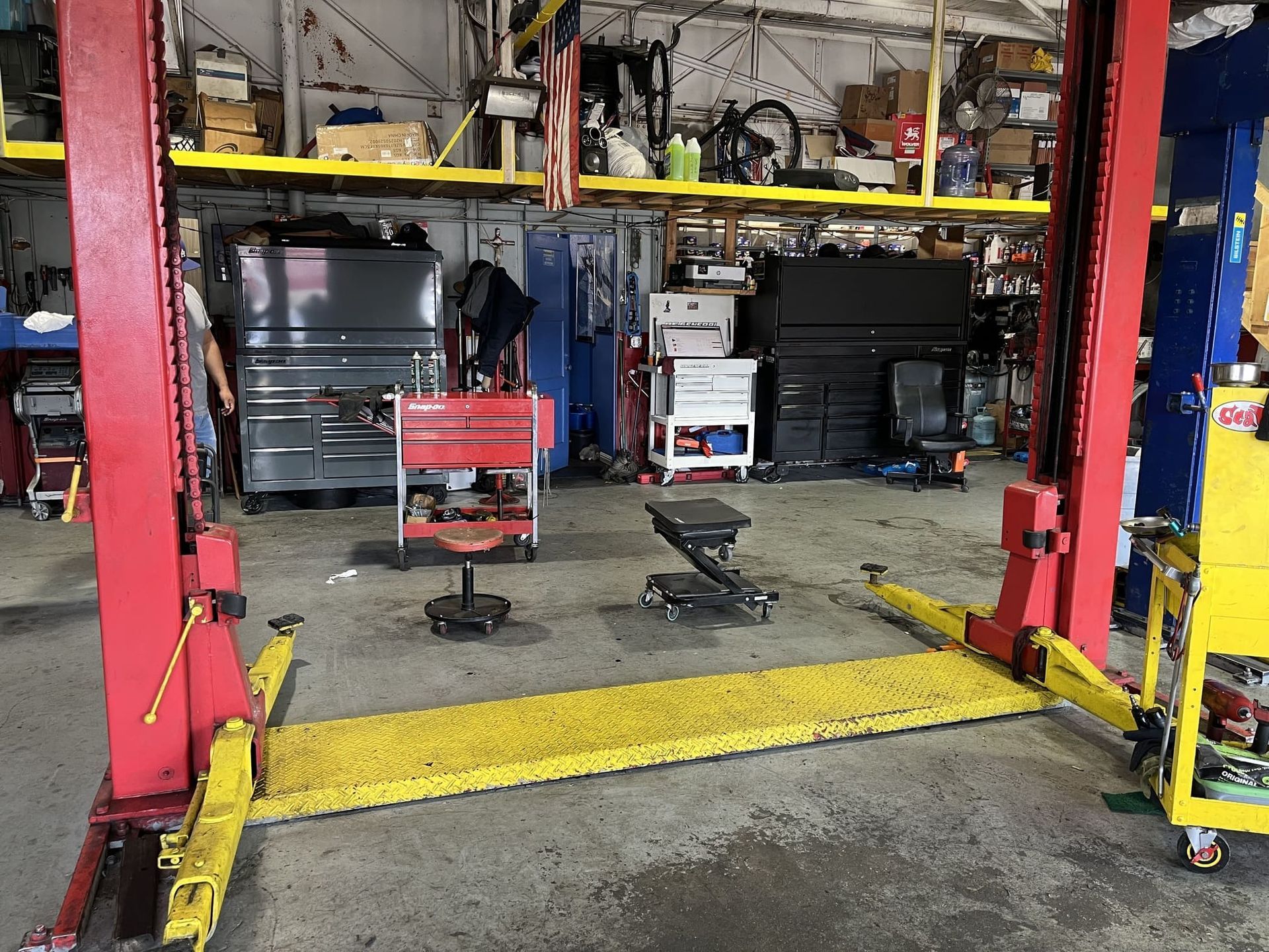 Auto repair shop with a red car lift, yellow arms, and stacked equipment in the background
