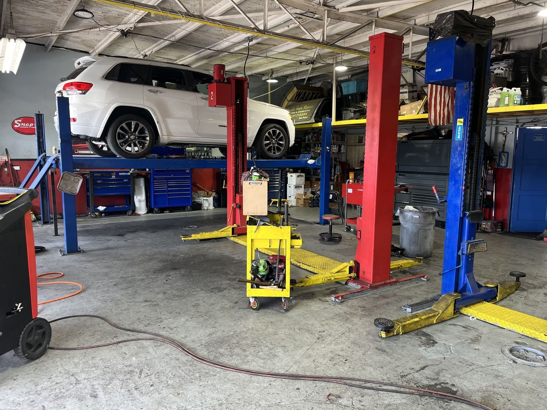 Auto repair shop with a white SUV on a lift and red-blue hydraulic equipment around it