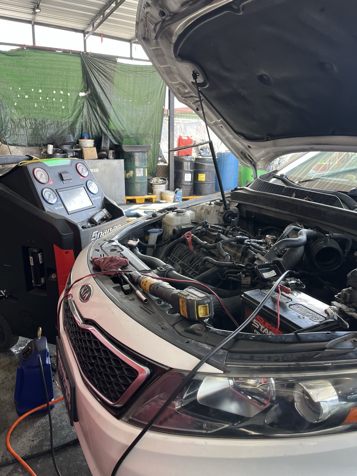 Car with hood open in a garage, engine exposed and diagnostic equipment beside it.