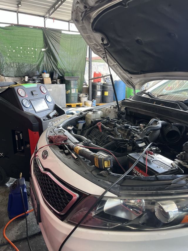 Car with hood open in a garage, engine exposed and diagnostic equipment beside it.