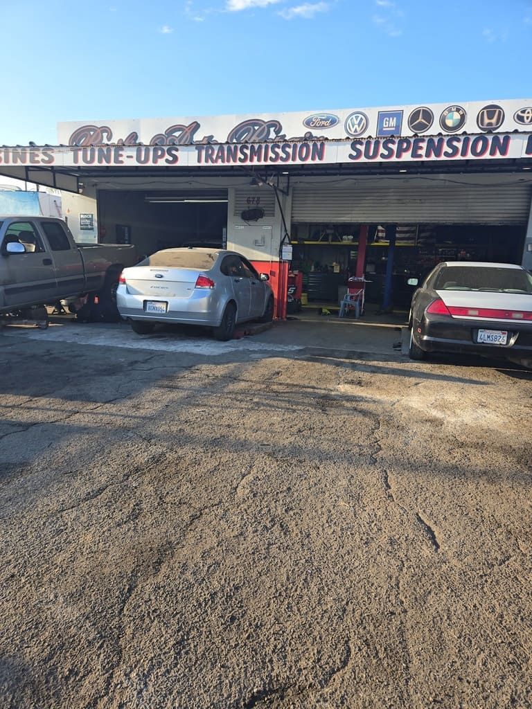Auto repair shop with several parked cars under a sign for tires, tune-ups, transmission, and suspension.
