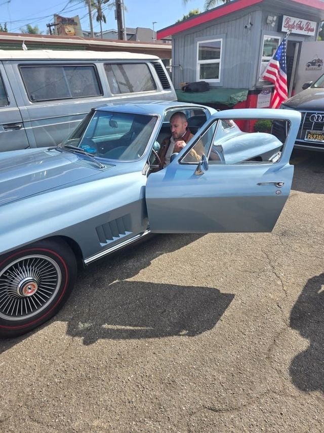 Light blue classic convertible with driver door open; man seated inside at a car show.