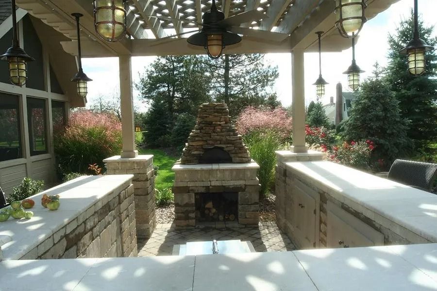 Outdoor kitchen with a stone pizza oven, built-in countertops, and hanging lanterns under a pergola.