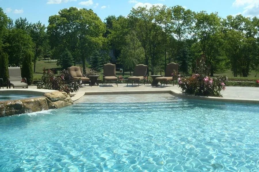 Pool with clear water, stone waterfall, and patio furniture on a sunny day.