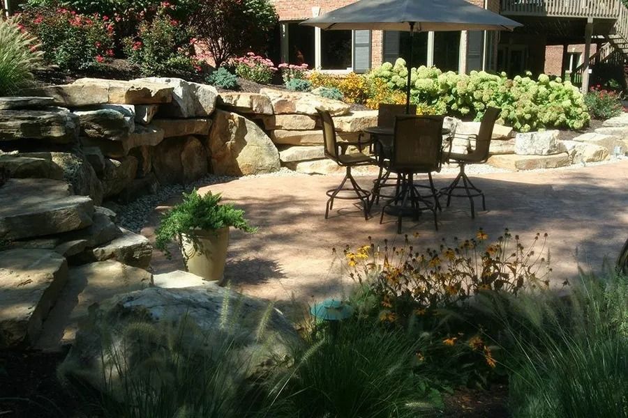 Backyard patio with stacked stone, table, and landscaping.