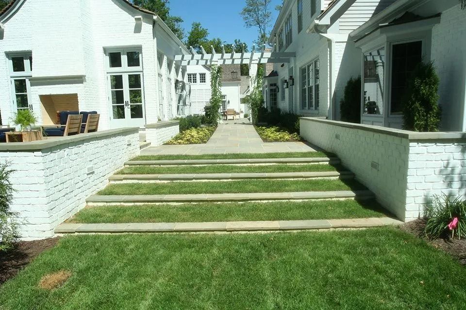 White building facade with stone steps and green grass leading to an archway.