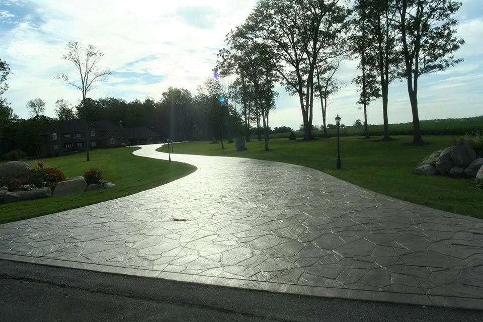 Long, curving concrete driveway leading to trees and a green lawn.