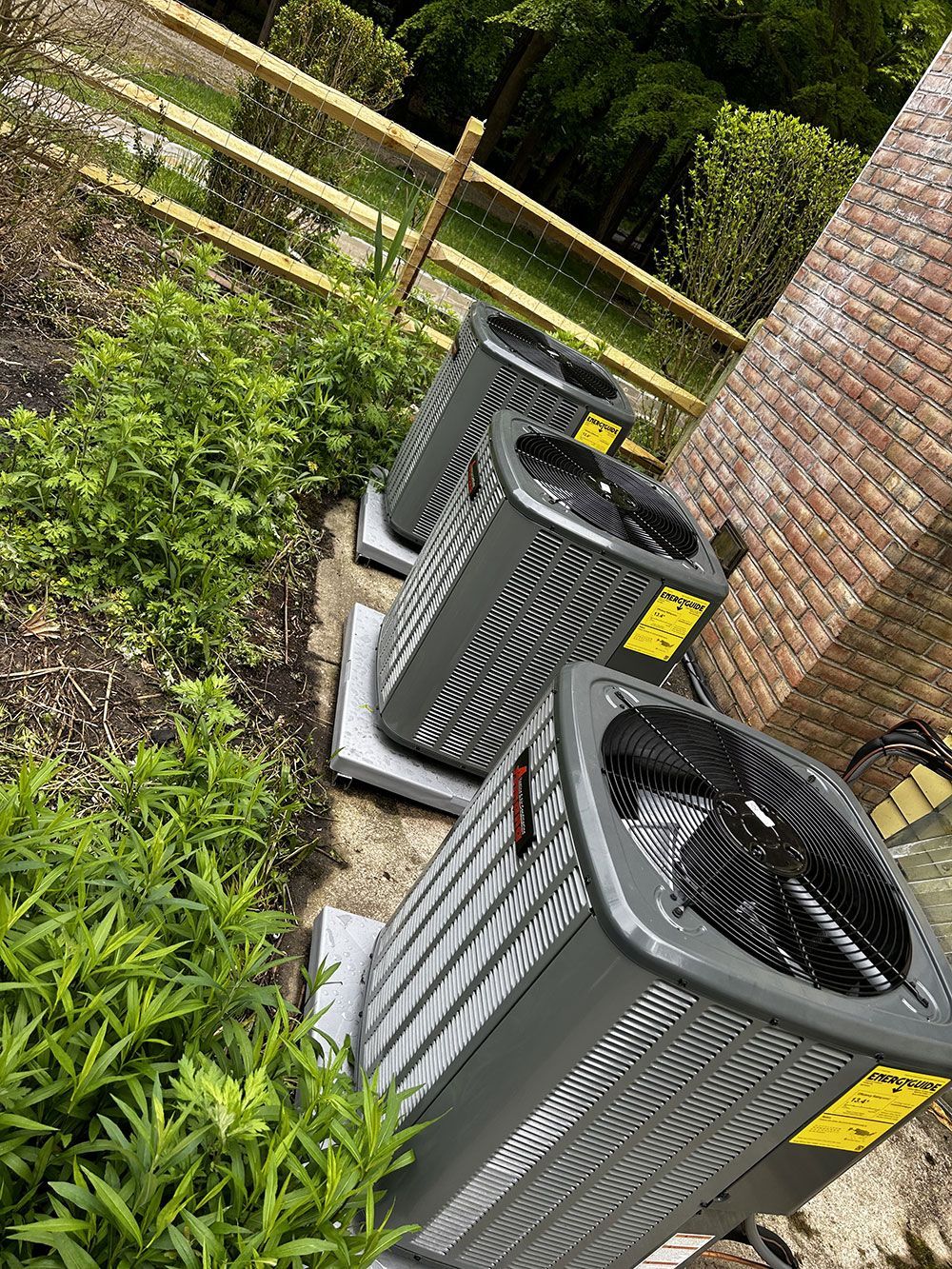 Three air conditioners are sitting next to each other in a garden.