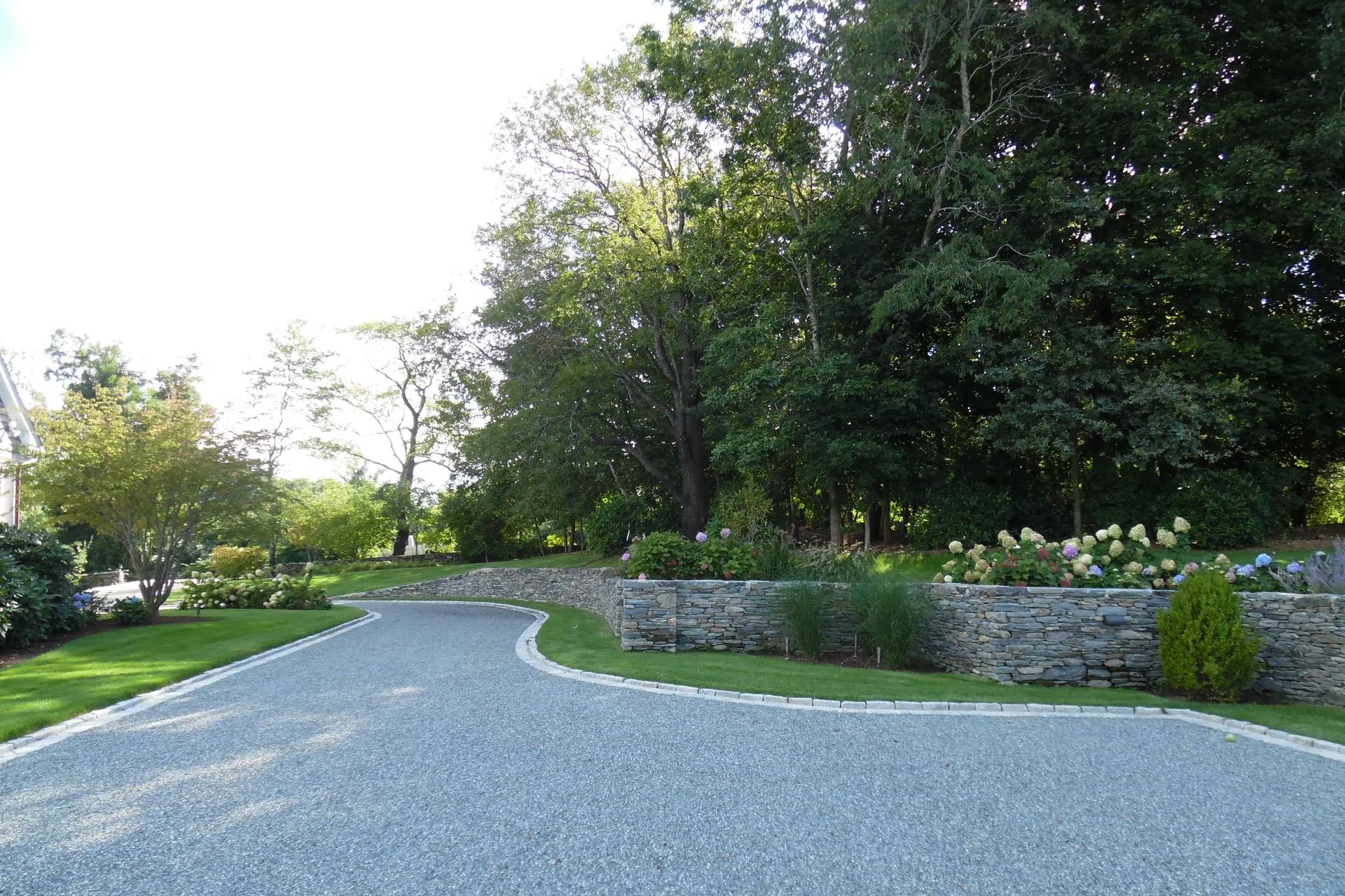 A gravel driveway with a stone wall on the side of it
