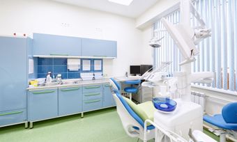 Bright dental clinic with blue cabinets, chair, and equipment near a large window