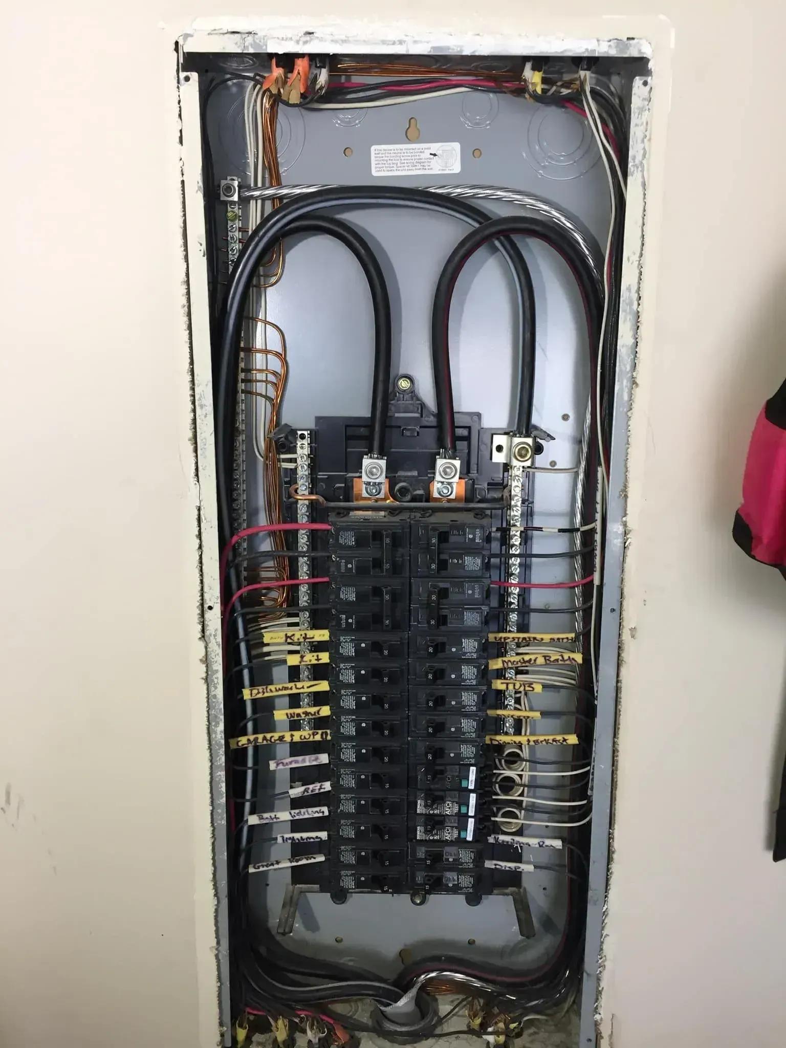 Electrical panel inside a wall, with wires, circuit breakers, and bus bars visible