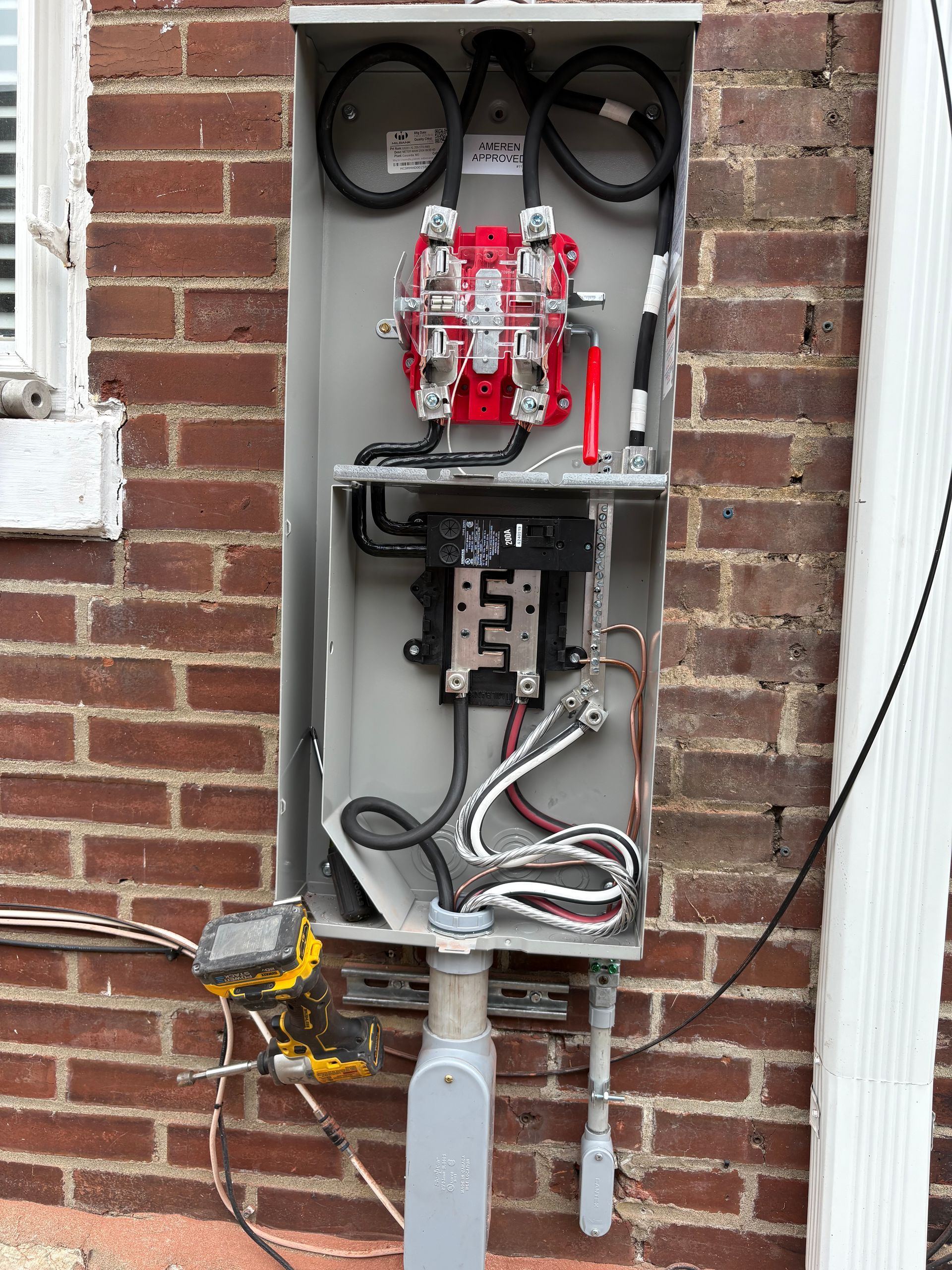 Open electrical panel on a brick wall with wires, breakers, and a meter socket.
