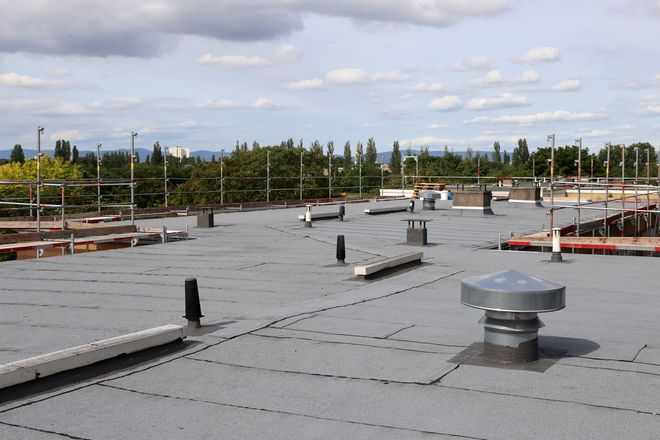 Flat commercial rooftop with gray membrane, vents, and safety rails under a cloudy sky
