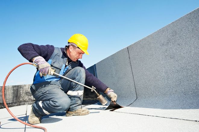 Worker in yellow hard hat sealing a rooftop seam with a caulking gun