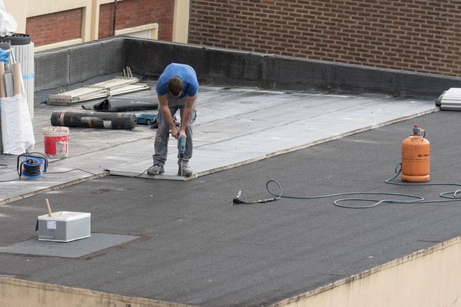 Worker repairing a flat rooftop with tools and an orange propane tank