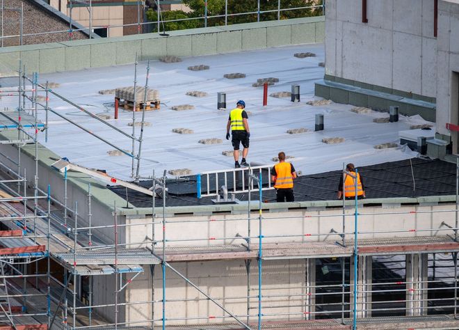 Workers in safety vests on a rooftop construction site with scaffolding and concrete slabs