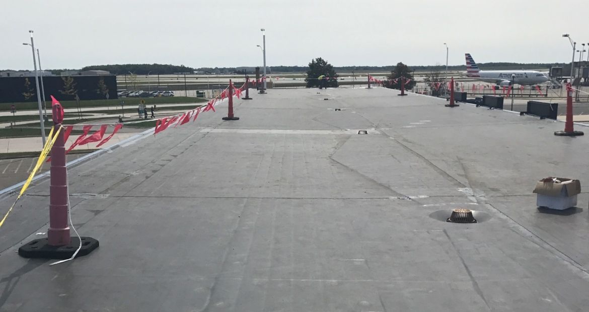 Rooftop under construction with red caution tape, poles, and scattered equipment on a flat concrete surface.