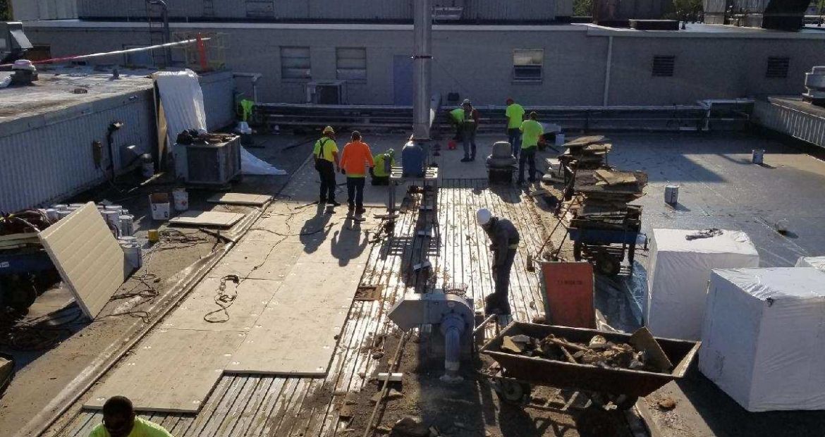 Workers in safety vests on a rooftop construction site beside materials and equipment