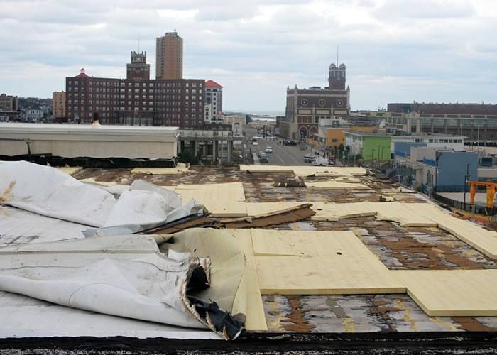 Rooftop under construction with white tarps, lumber, and city buildings in the background.