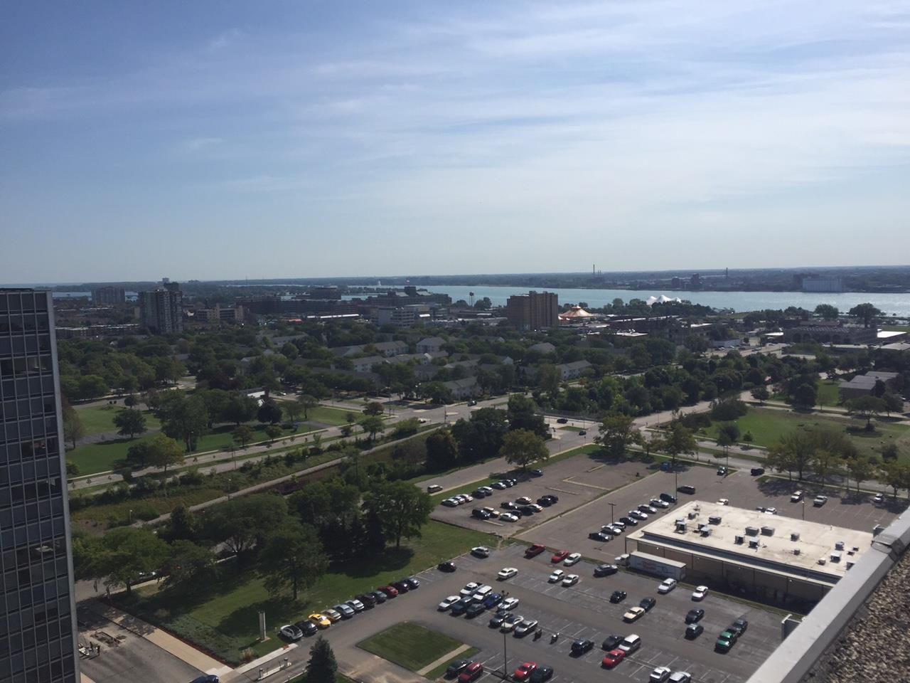 Aerial view of a parking lot, trees, roads, and a waterfront cityscape under a clear sky